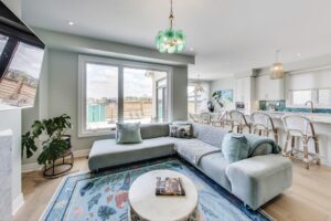 Bright living room at 59 Maskells Cres with large window, teal sectional, and open flow to the kitchen island.